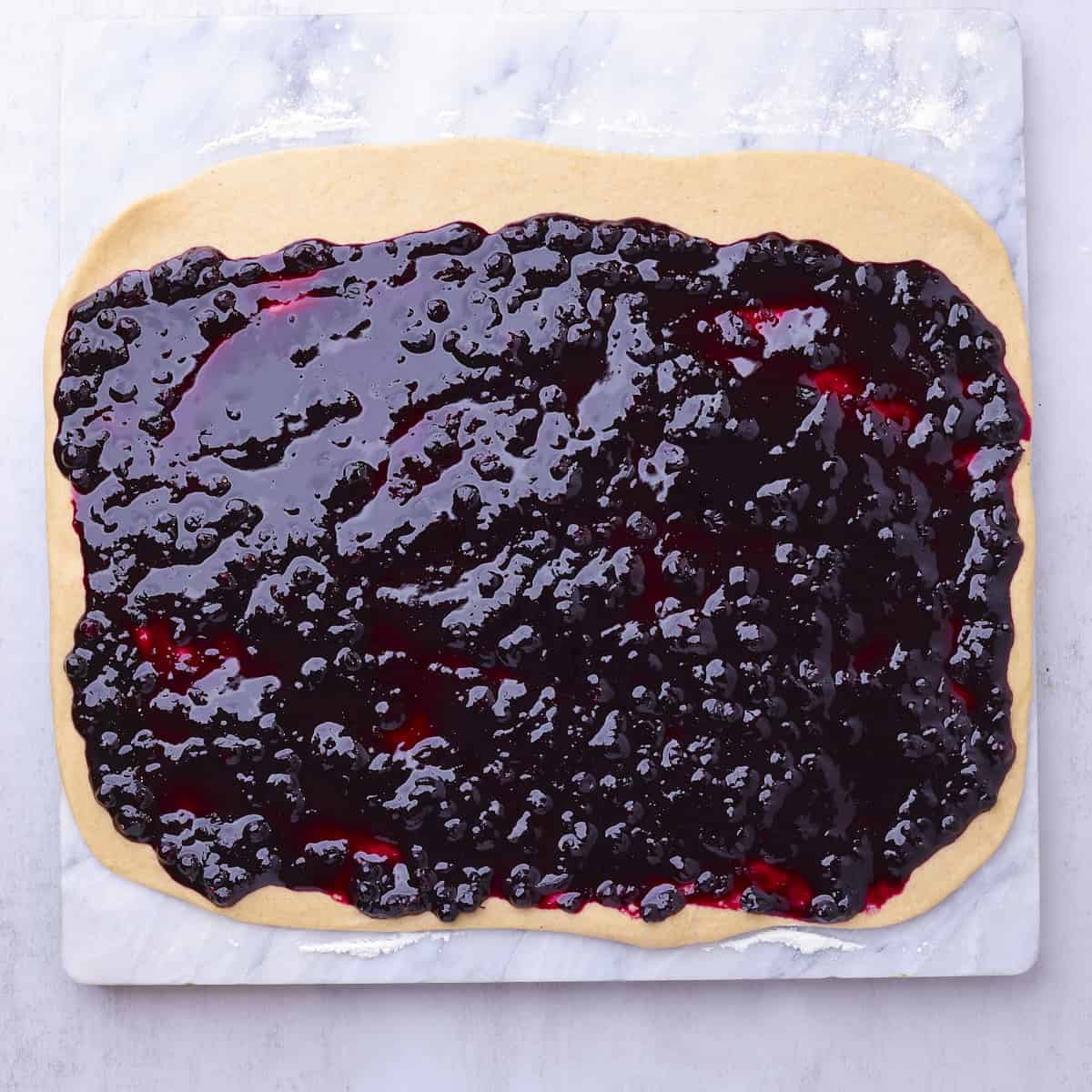 The blueberry cinnamon rolls dough rolled out into a rectangle with the filling spread over it with a border at the top.