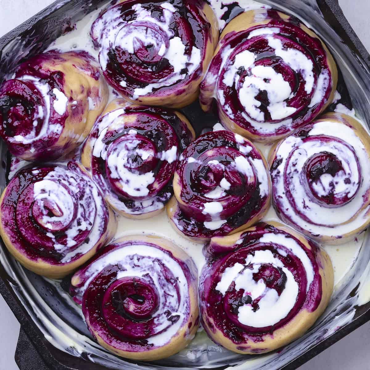 The risen rolls in the skillet with heavy cream poured over them.