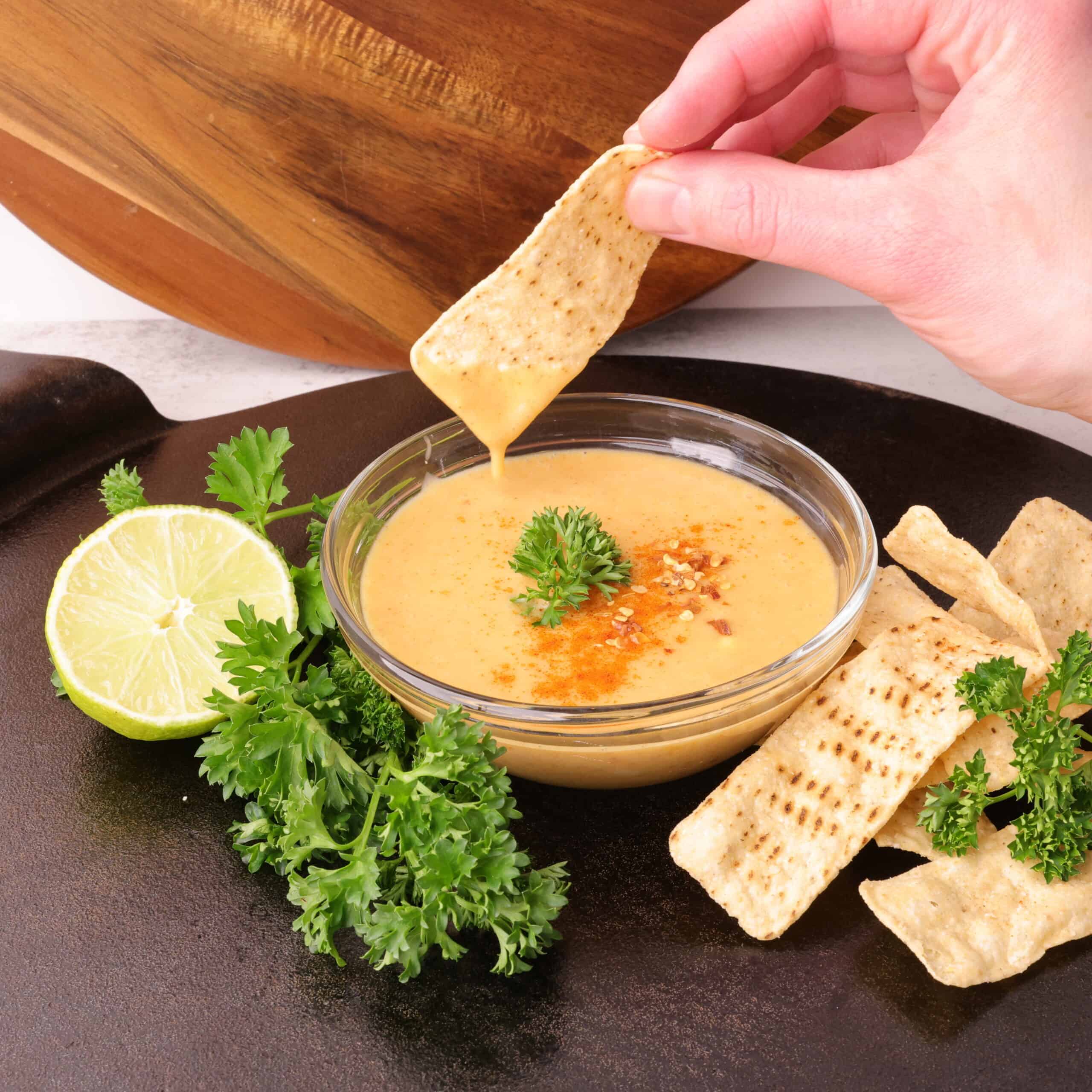 A bowl of the Honey Mayo Mustard Sauce on a cast iron platter with greens, a lime and chips beside it.