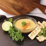 A cast iron platter with a bowl of Honey Mustard Mayo Sauce on it with greens and a lime on one side and chips for dipping on the other.