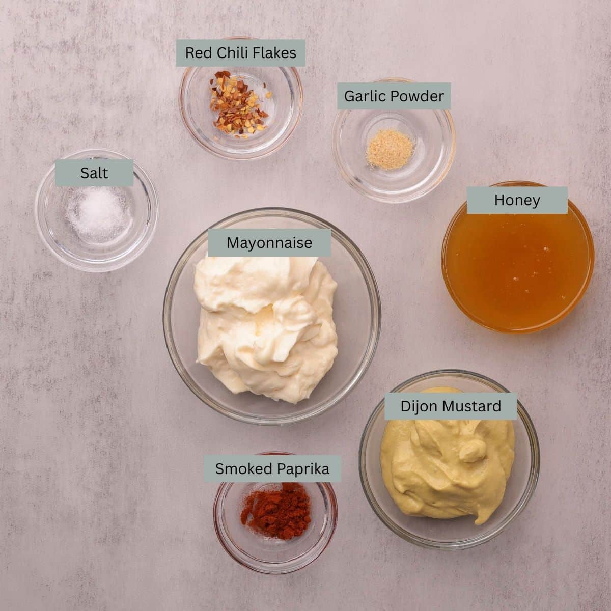 A visual display of the ingredients needed for the Honey Mayo Mustard Sauce - mayonnaise, honey, Dijon mustard, salt, garlic powder, smoked paprika and red chili flakes - each in their own bowl.