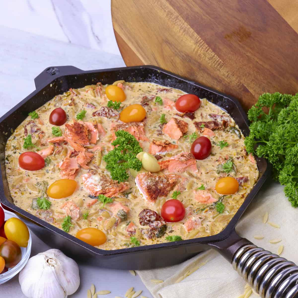 A skillet filled with the finished Salmon Pasta, garnished with parsley and fresh cherry tomatoes.