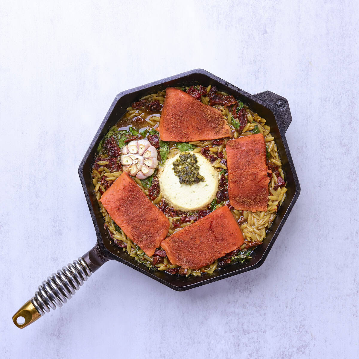 A skillet with the partially baked pasta topped with the raw salmon fillets.