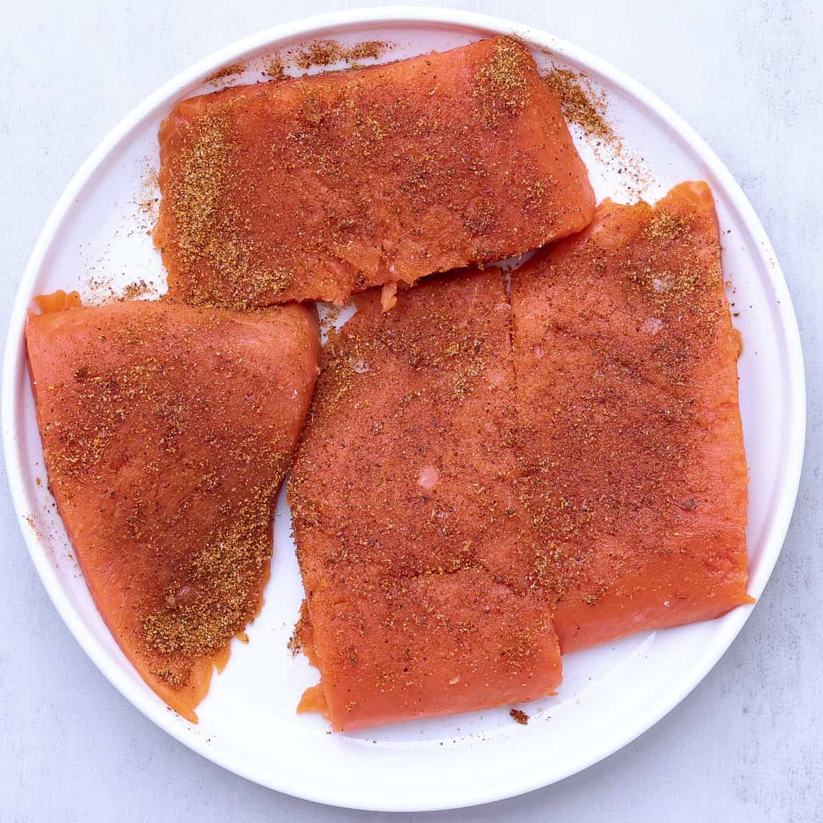 The salmon fillet cut into four equal pieces and topped with blackened seasoning.