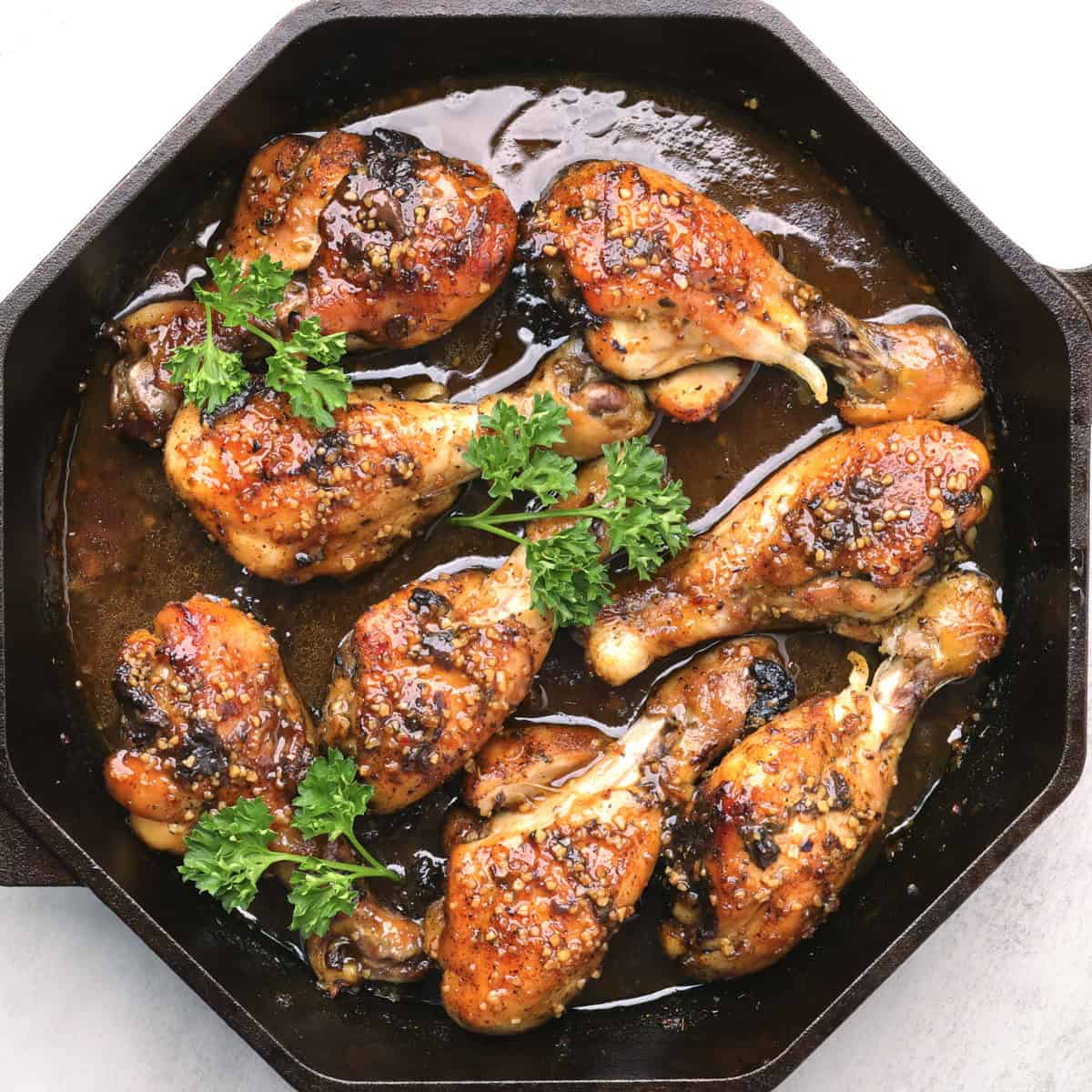 A skillet with baked Sticky Chicken Drumsticks garnished with greens.
