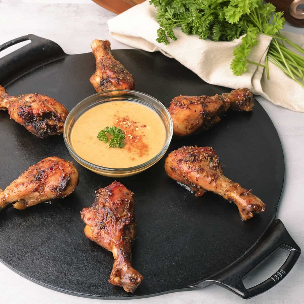 A cast iron platter with a bowl of honey mustard sauce in the center and Sticky Chicken Drumsticks circled around it.