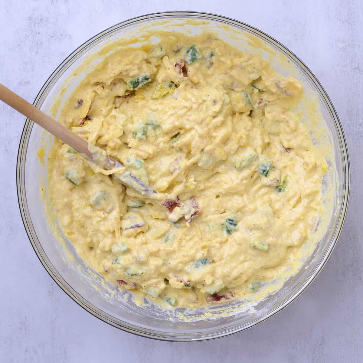 A bowl with the fillings in the batter with a wooden spoon in the bowl.