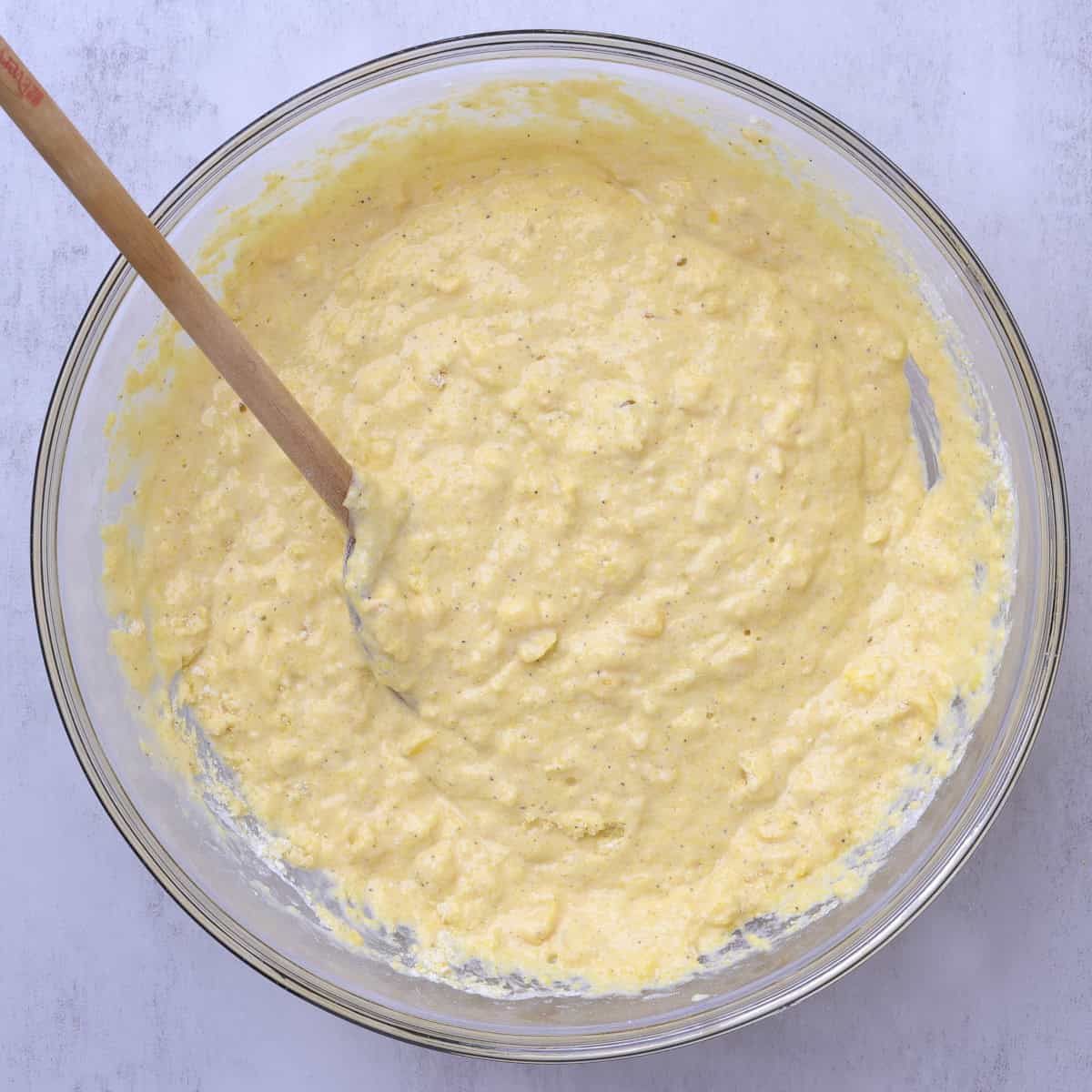 A bowl with the combined batter in it with a wooden spoon.