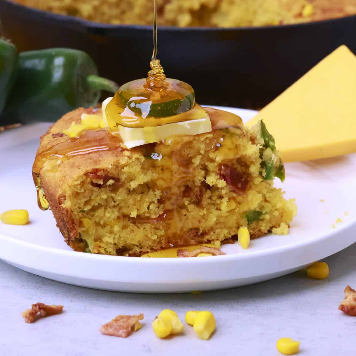 A slice of Cheddar Cheese Jalapeno Cornbread on a plate with syrup pouring over it.