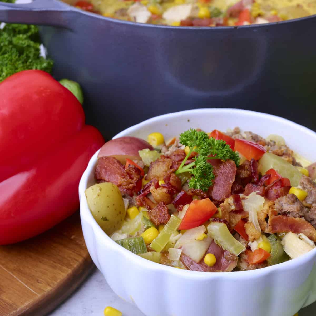 A close up of the soup in a white bowl with the pot of soup in the background and a bell pepper beside.
