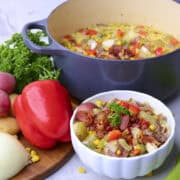 The Chicken and Sausage Soup displayed in the cast iron pot and in a white bowl with a variety of vegetables displayed beside.