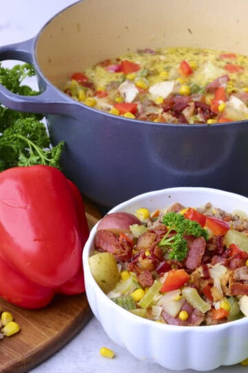 The Chicken and Sausage Soup displayed in the cast iron pot and in a white bowl with a variety of vegetables displayed beside.