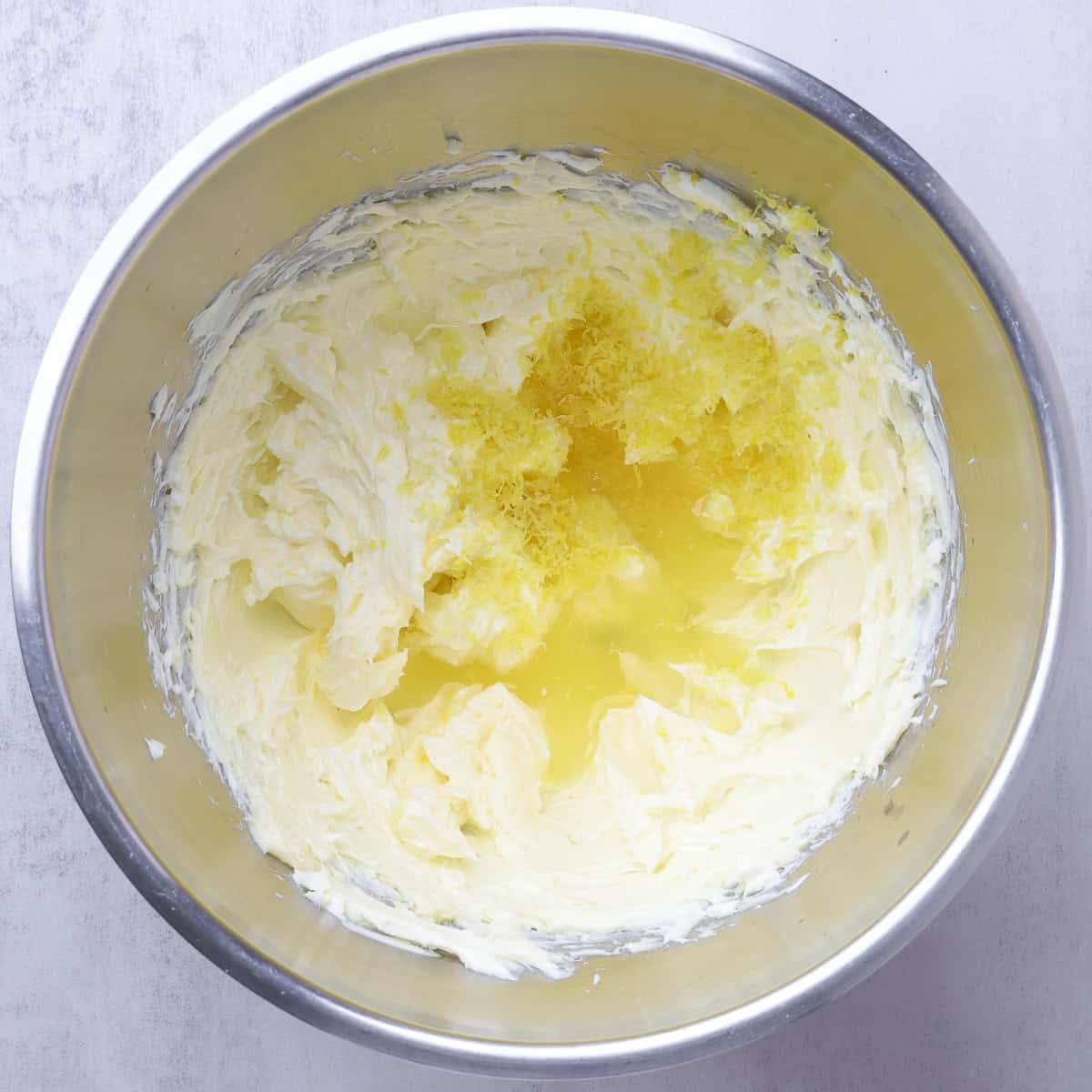 The mixing bowl containing the beaten butter and cream cheese with the salt, liquids and zest on top, ready to mix in.