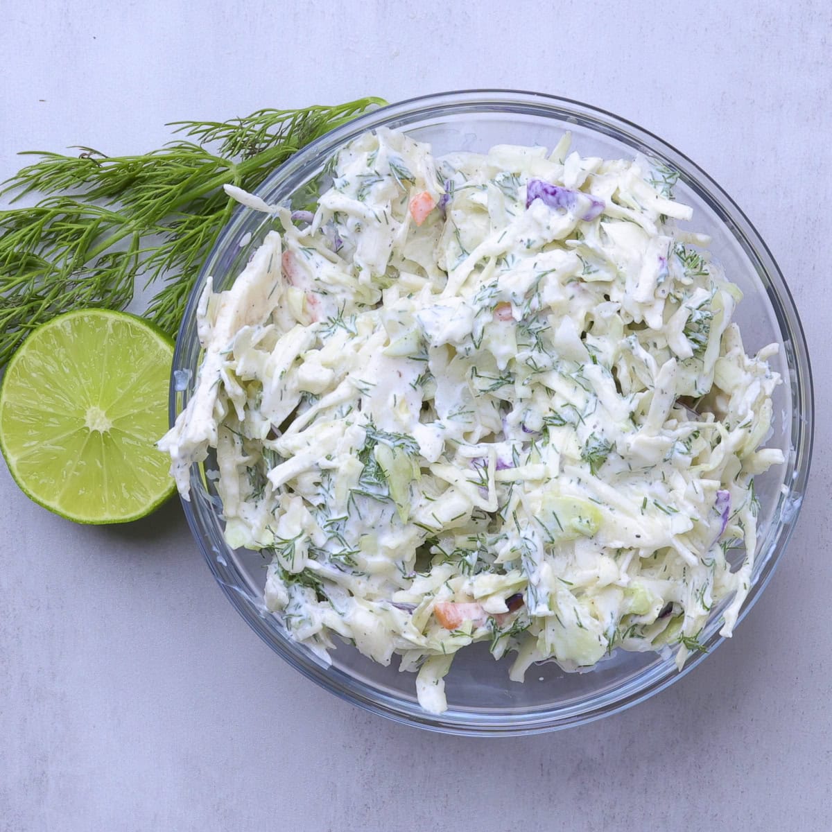 A bowl of dressed coleslaw with a cut lime and sprig of dill beside.
