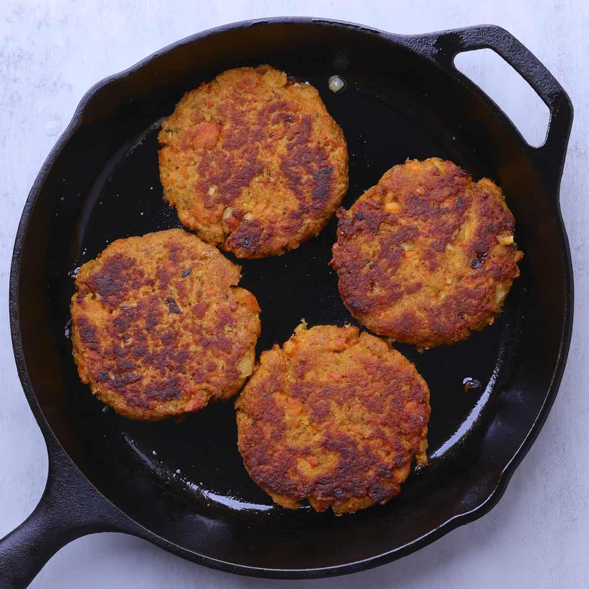 A skillet with four cooked Smoked Salmon Patties in it.