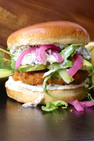A Salmon Burger made with Canned Salmon with toppings displayed with lime, lemon and avocado.