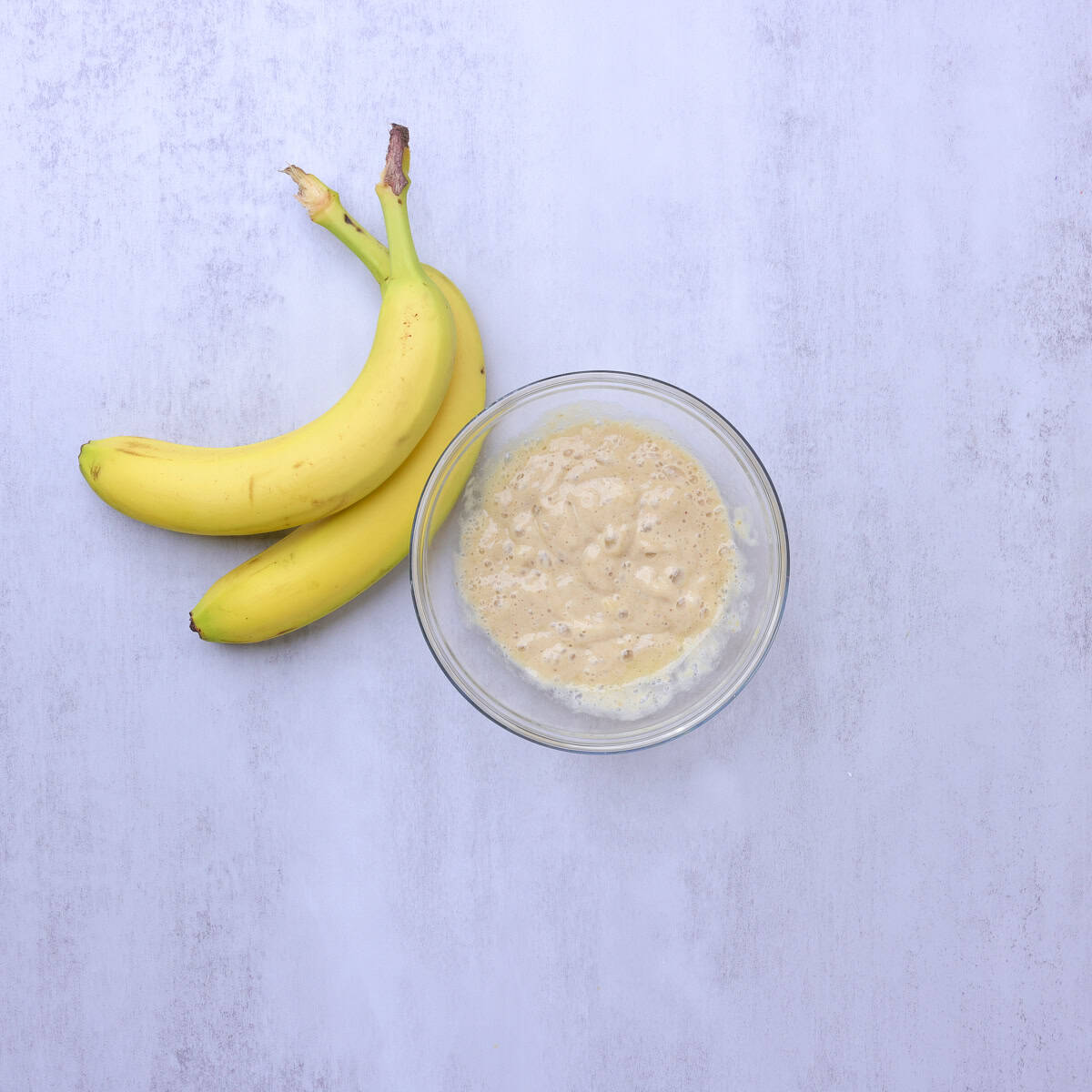 A bowl filled with banana puree. Displayed with bananas.