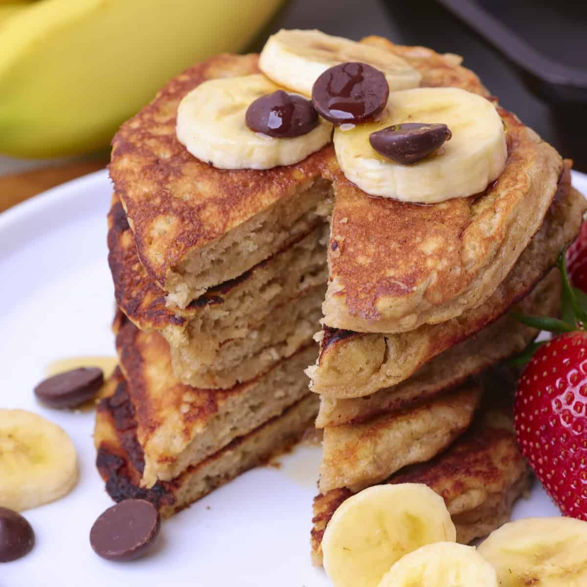 Sourdough Banana Pancakes stacked on a plate with a slice removed and topped with sliced bananas and chocolate chips.