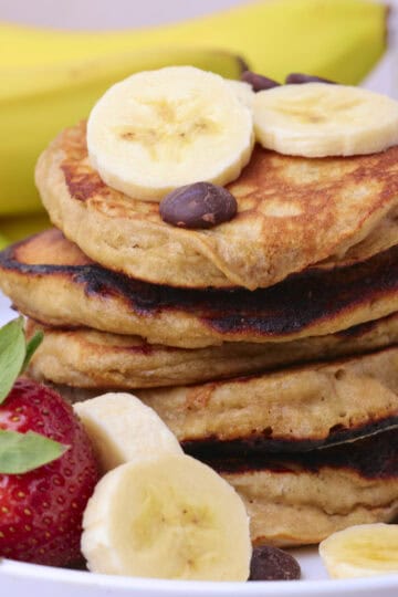 Sourdough Banana Pancakes Stacked on a plate and displayed with fruit and chocolate chips.
