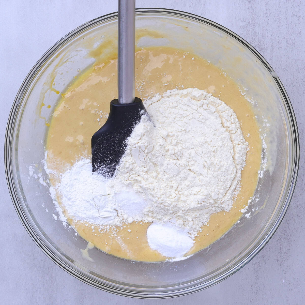 A glass bowl with the dry ingredients poured on top of the wet ingredients. 