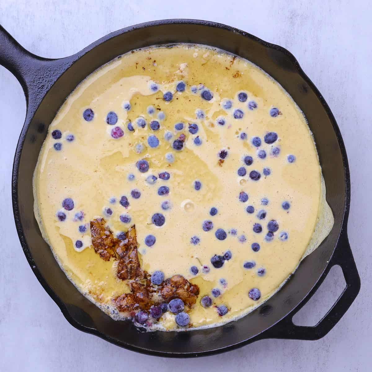 A hot skillet filled with the pancake batter and sprinkled with blueberries.