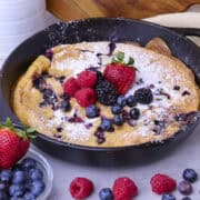 A golden Sourdough German Pancake in the skillet dusted with powdered sugar and topped with fresh berries.