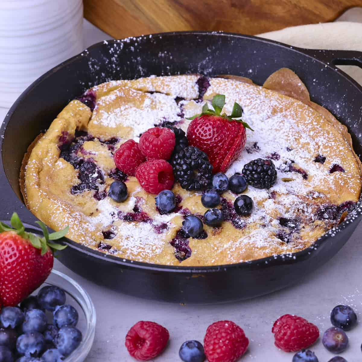 A golden Sourdough German Pancake in the skillet dusted with powdered sugar and topped with fresh berries.