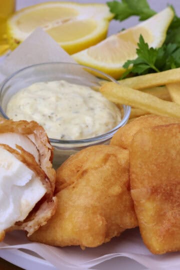 Beer Battered Halibut displayed on a plate, one piece open faced, with tartar sauce and fries.