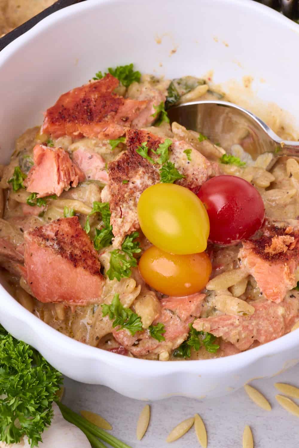 Salmon with Pasta served in a bowl with a spoon and three tomatoes.