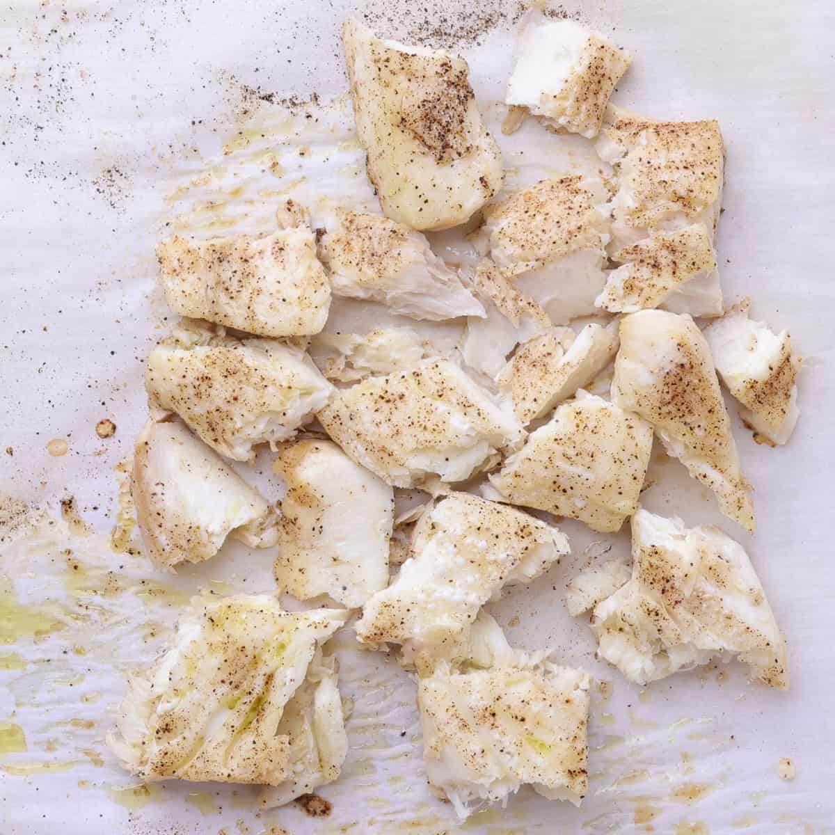 Baked halibut flaked into pieces on parchment paper.