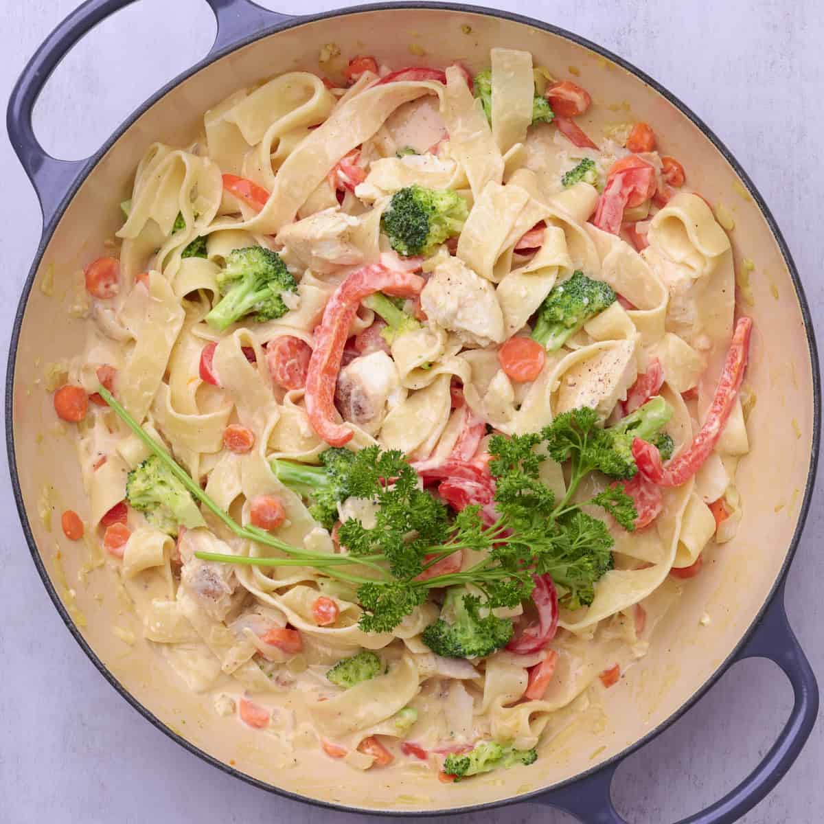 A large pot full of the finished halibut pasta with all the noodles and veggies combined and topped with creamy Alfredo sauce.