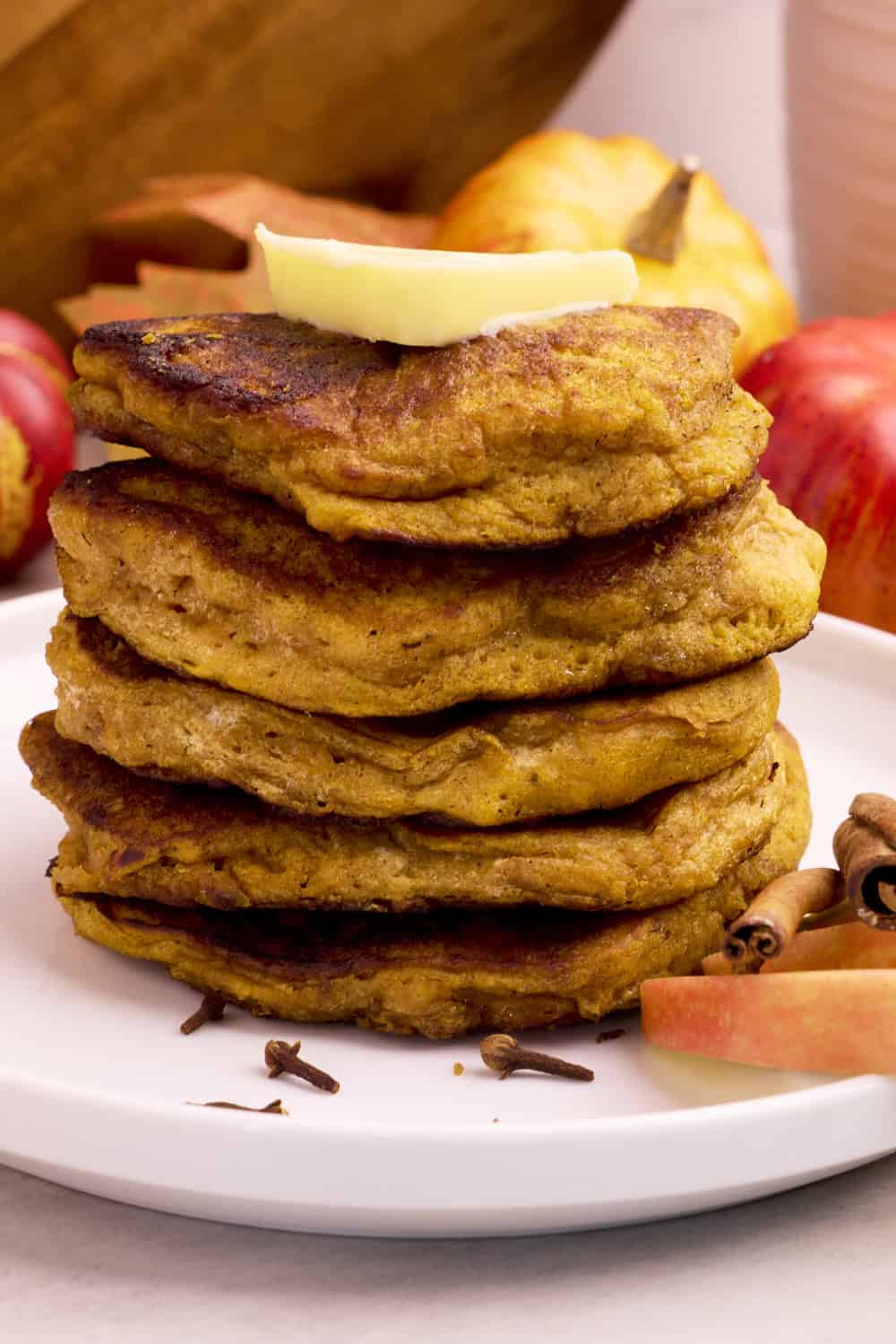 A white plate stacked with Sourdough Pumpkin Pancakes topped with butter.