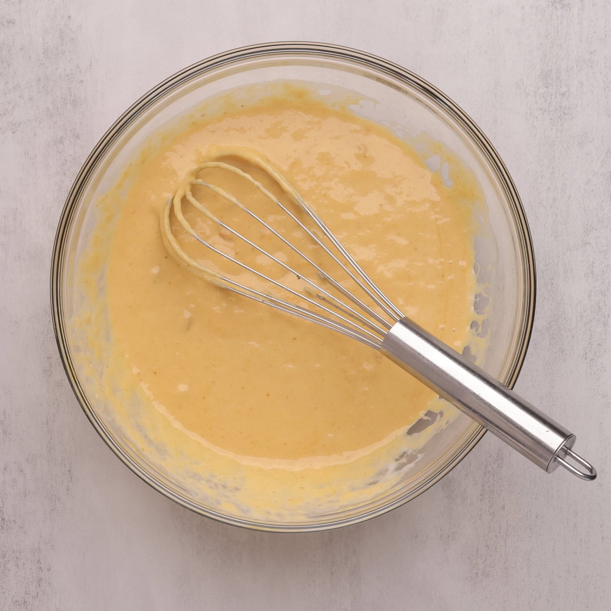 A glass bowl with the whisked wet ingredients and whisk.