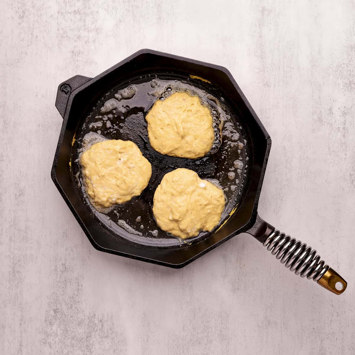 A skillet with hot butter and three pancakes cooking in it.