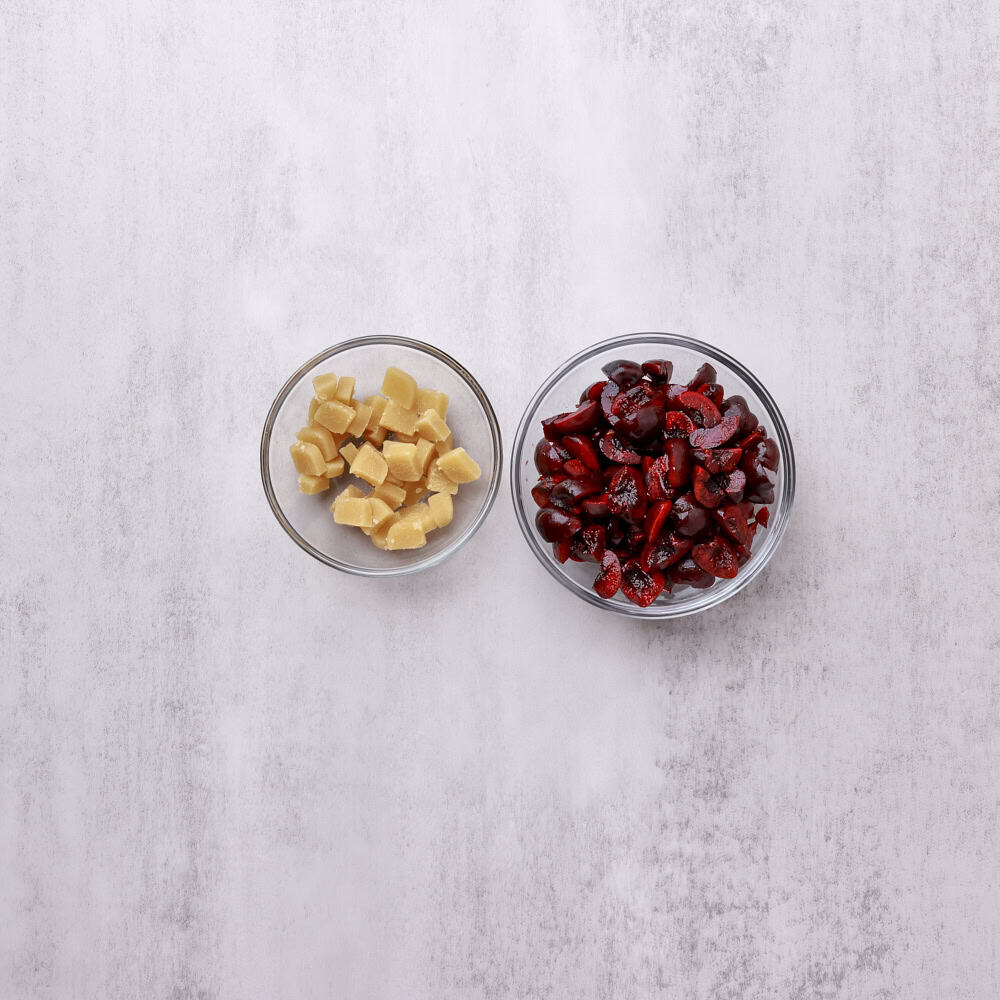 A bowl of diced marzipan and bowl of quartered cherries.