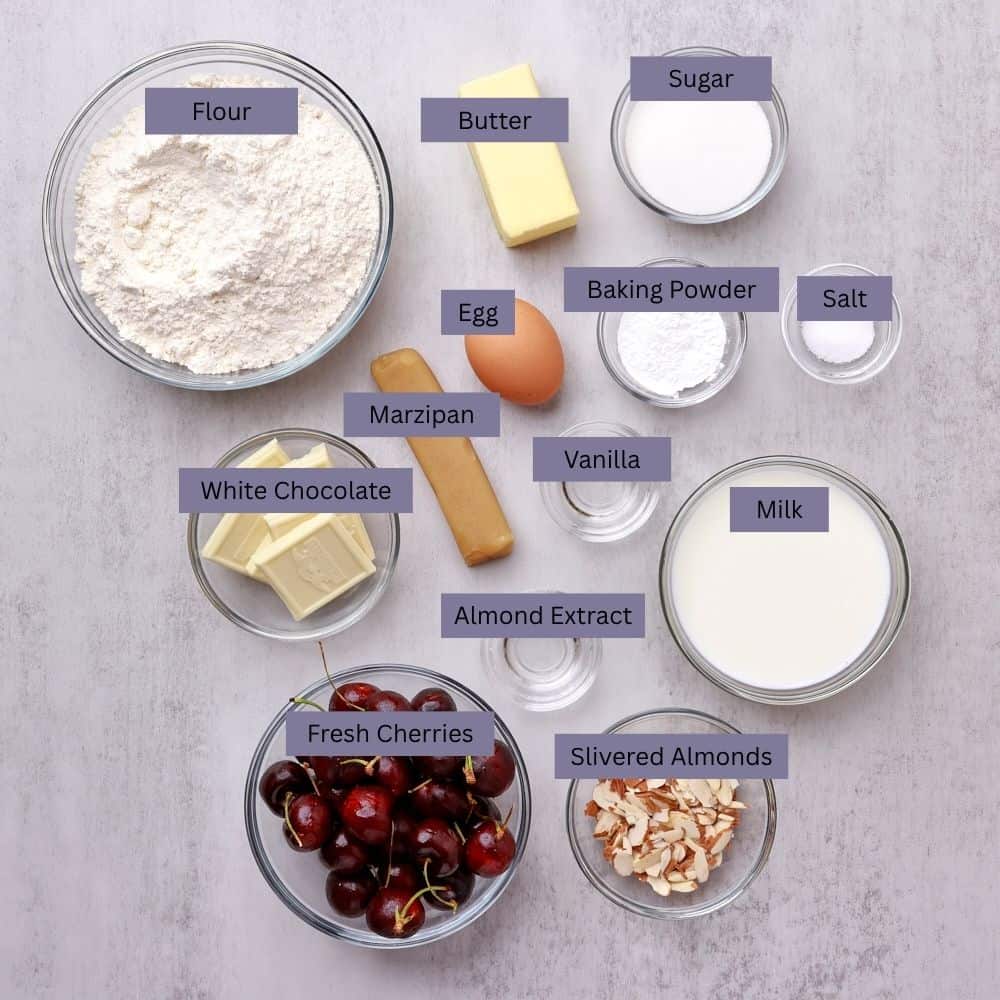 A visual display of the ingredients needed for the Cherry Scones - flour, butte,r sugar, marzipan, an egg, baking powder, salt, bakers white chocolate, vanilla, almond extract, milk, fresh cherries and slivered almonds - each displayed in their own bowl.