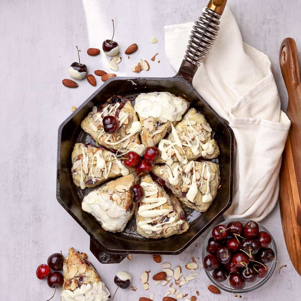 An overhead view of the cherry scones displayed in the skillet, drizzled in white chocolate and displayed with cherries and sprinkled almonds.