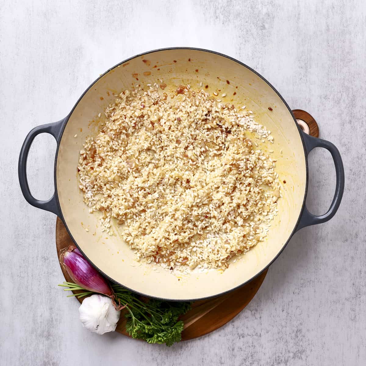 A large pan with the rice combined with the sauteed onions and garlic.
