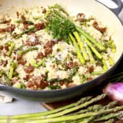 A pan filled with chorizo risotto, topped with full pieces of asparagus for garnish.