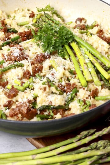 A pan filled with chorizo risotto, topped with full pieces of asparagus for garnish.