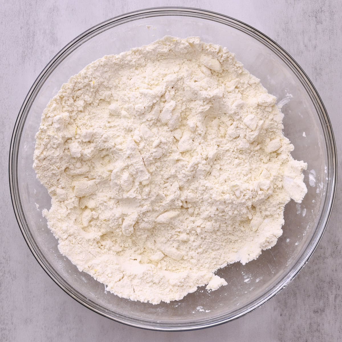 A glass bowl with the dry ingredients and butter cut in.