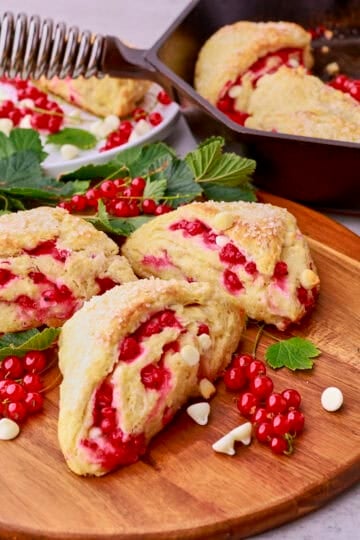 Three scones on a wooden board with a skillet of scones in the background.