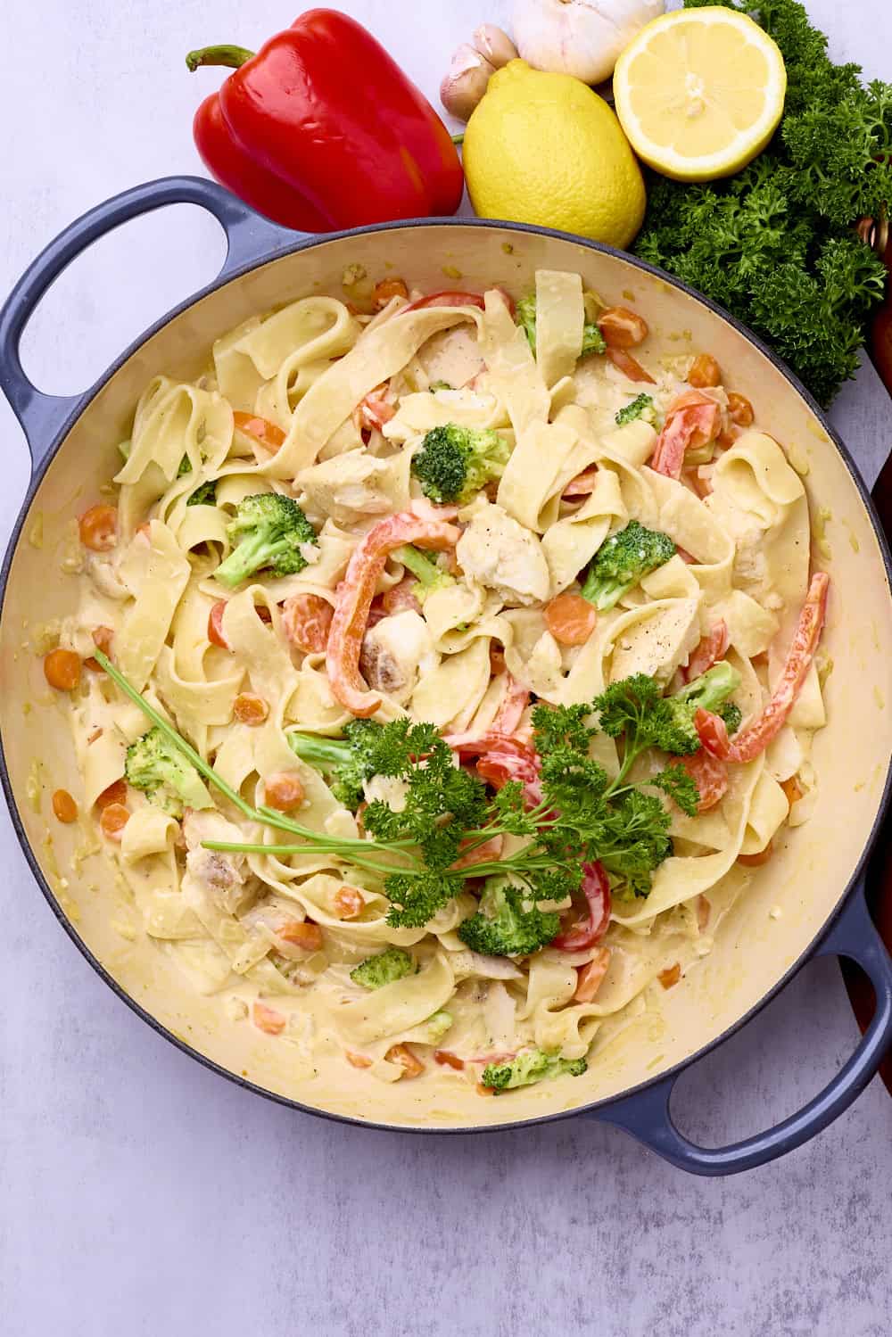 A pot of halibut pasta displayed with greens, a lemon and a red bell pepper.