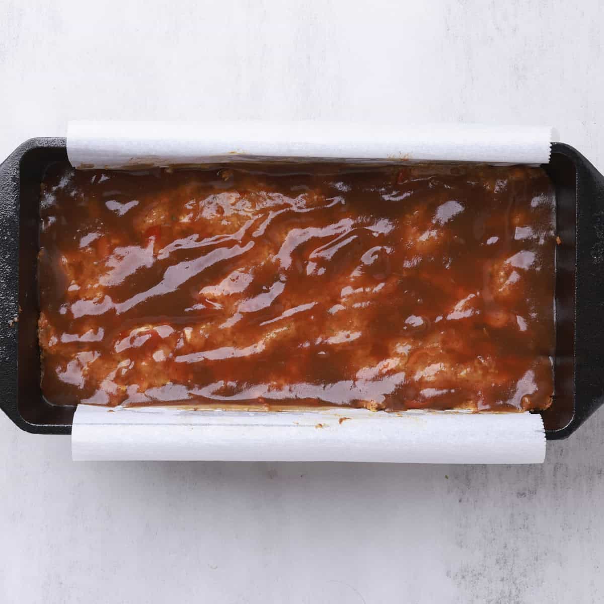 The salmon loaf in the pan with the barbecue sauce spread on it.