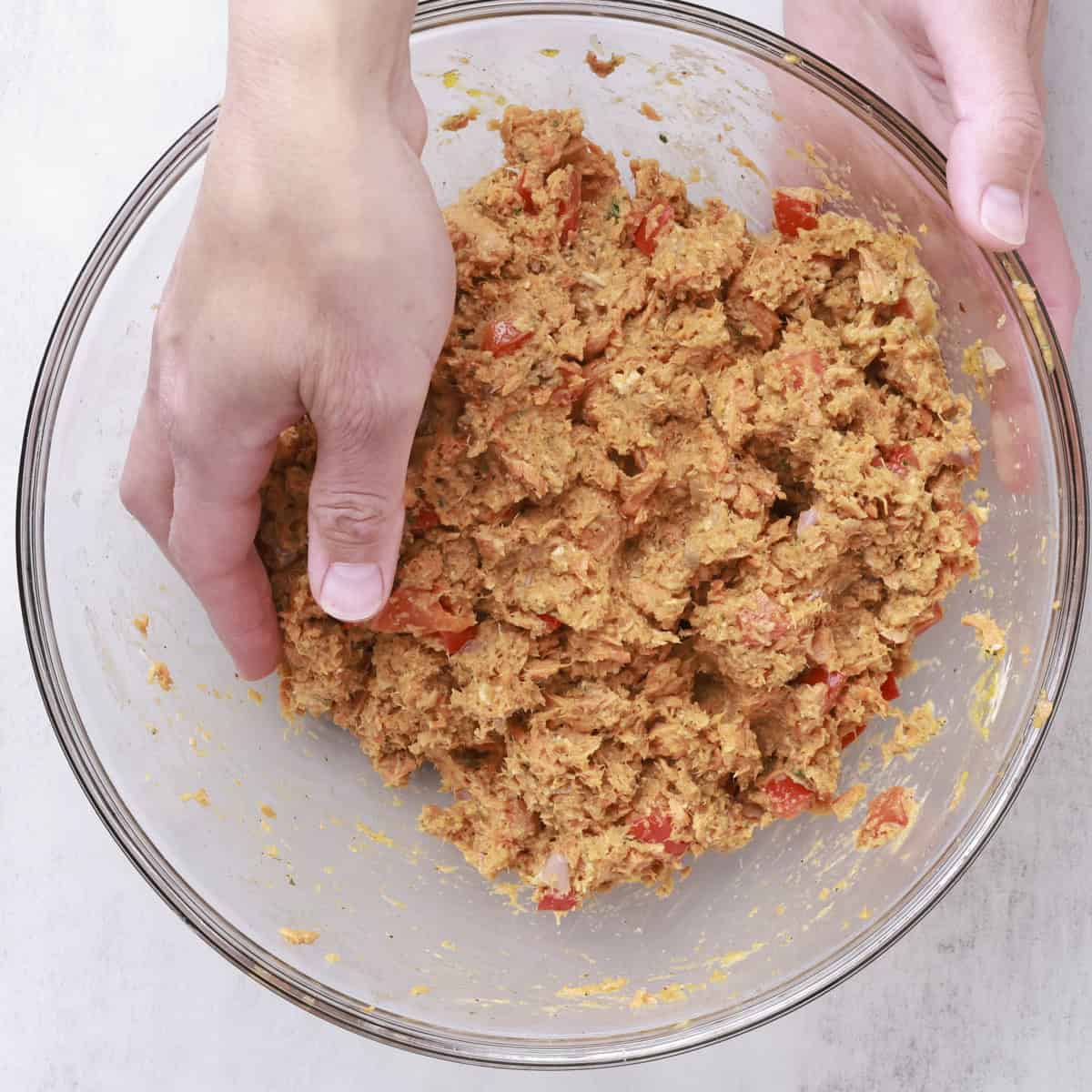 A glass bowl with a hand mixing together the ingredients for the salmon loaf.