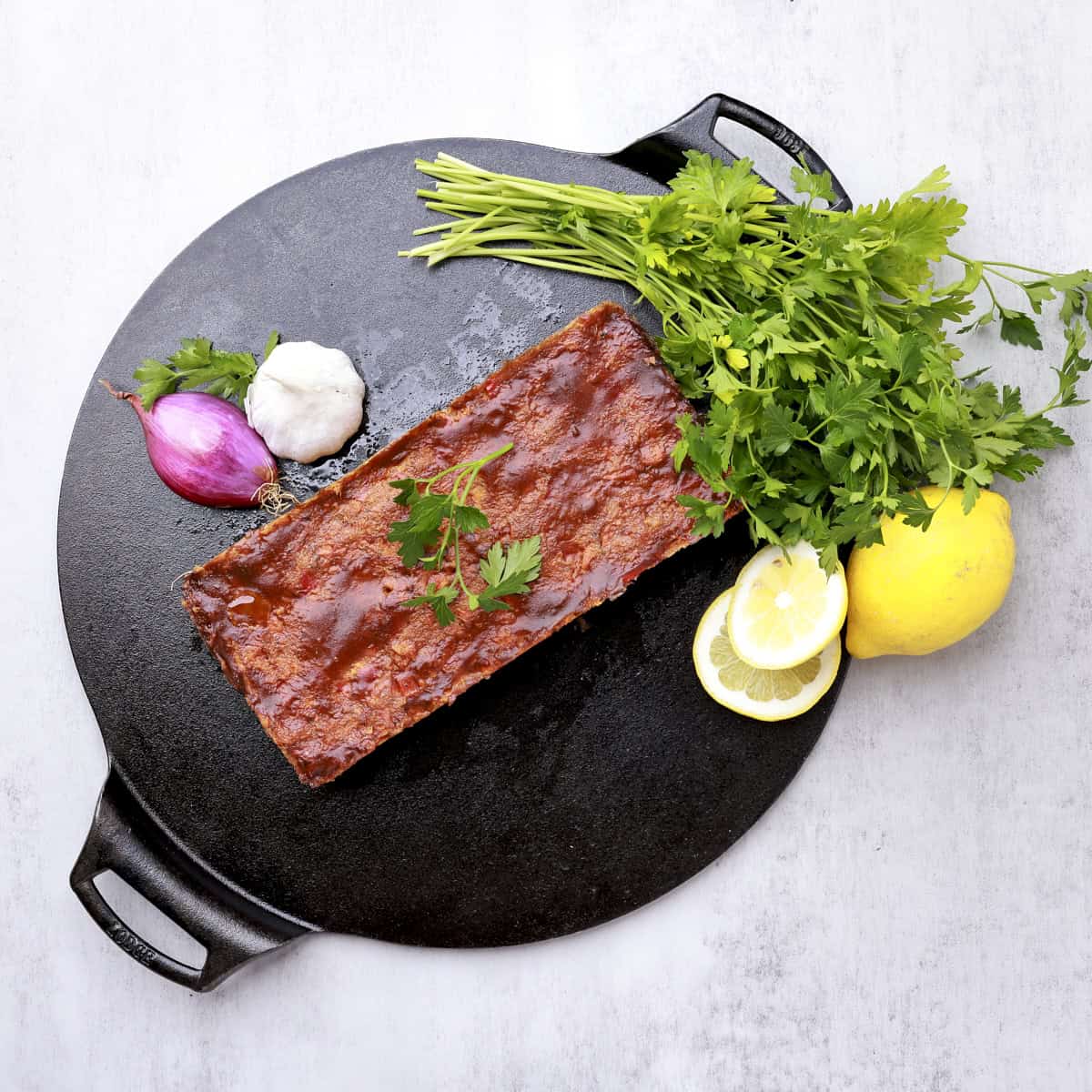 The Salmon Loaf displayed on a cast iron plate with greens, lemons, a shallot and garlic.