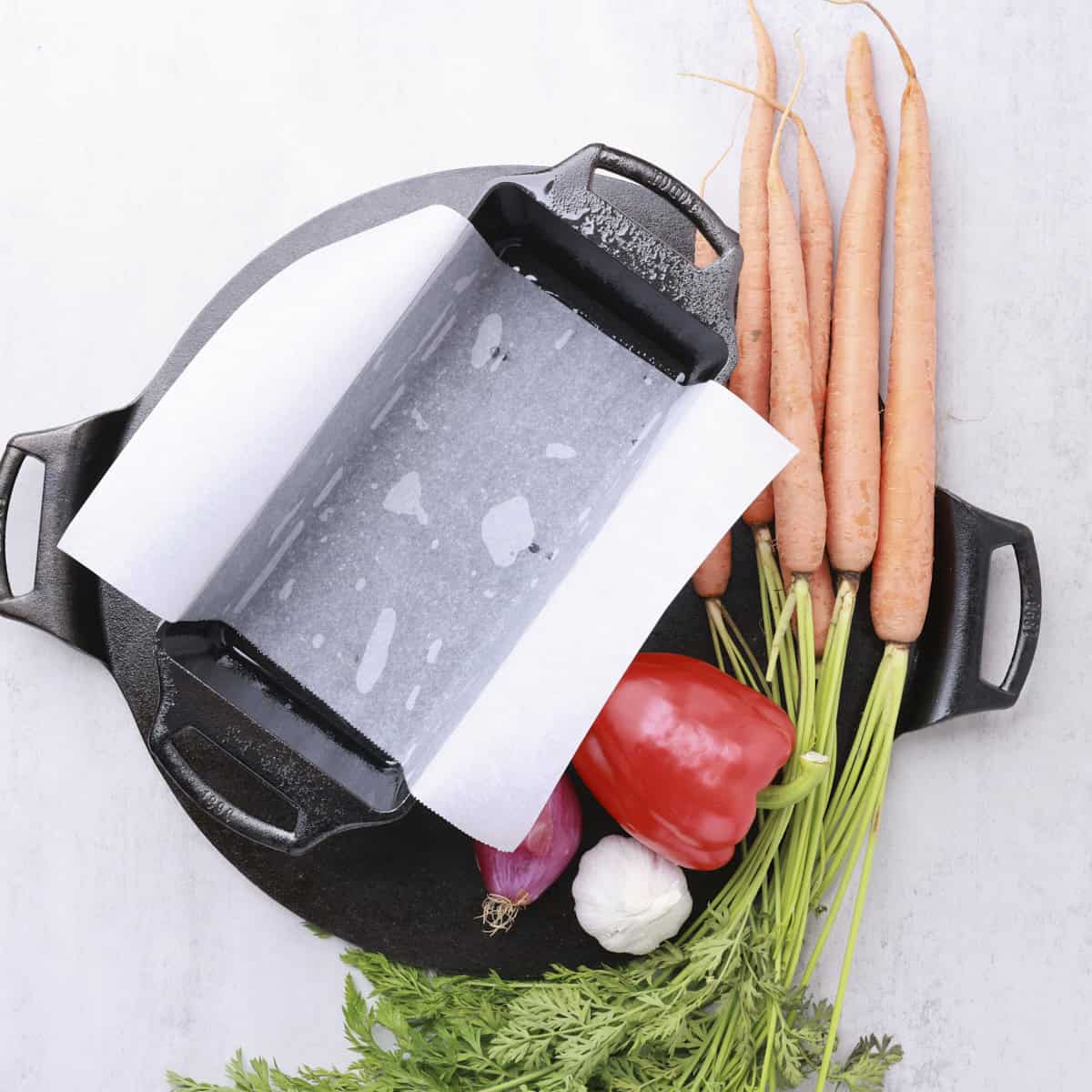 A cast iron loaf pan lined with parchment paper and displayed with veggies.