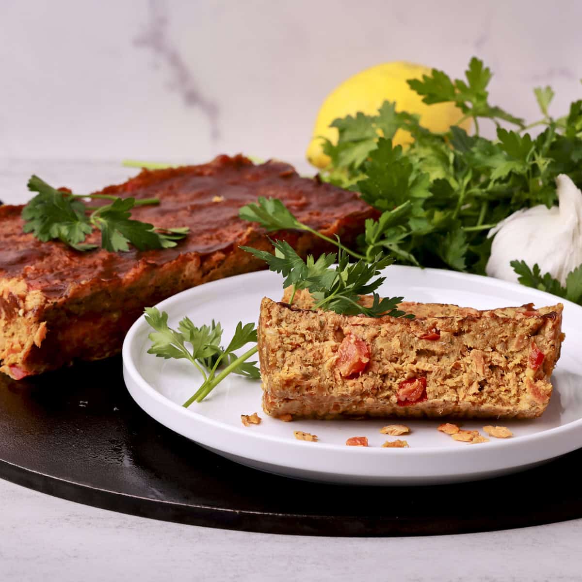 Slices of the salmon loaf on a white plate, garnished and with the remaining loaf in the background.