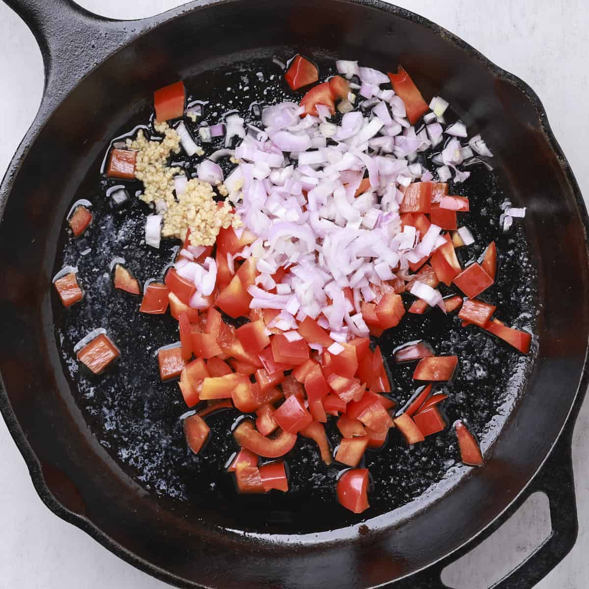 A skillet with bell peppers, shallots and garlic, ready to saute. 