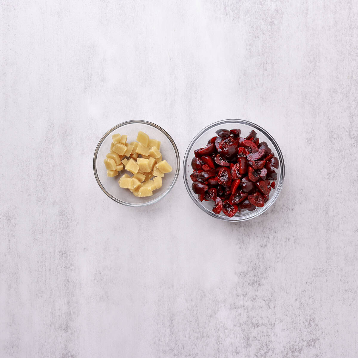 A bowl of diced marzipan and bowl of quartered cherries.